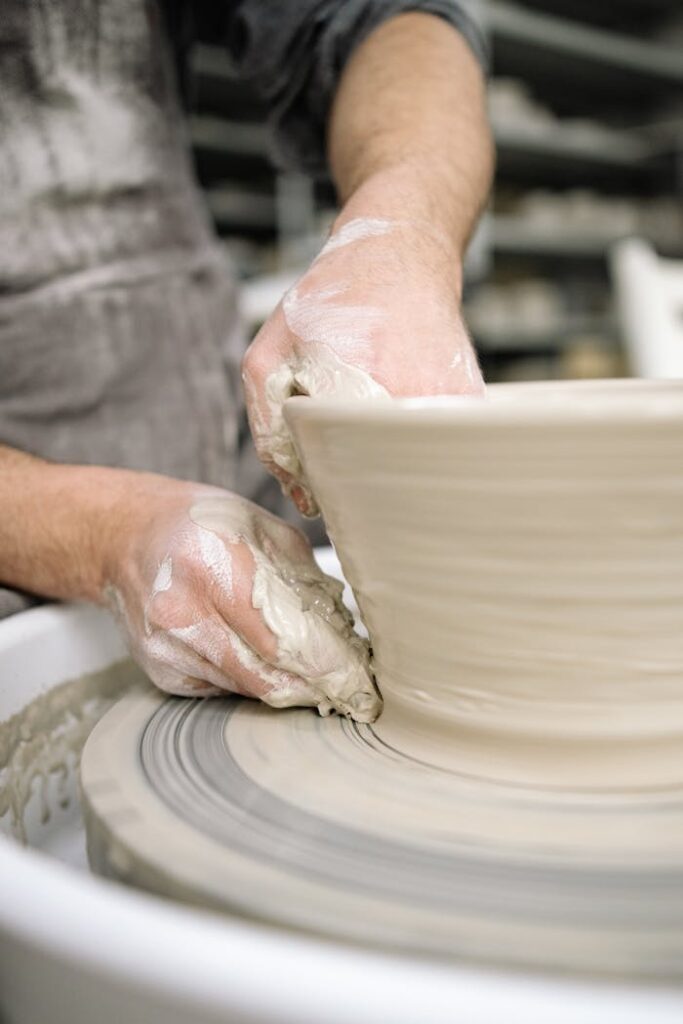 A detailed view of a potter's hands skillfully shaping clay on a pottery wheel indoors.
