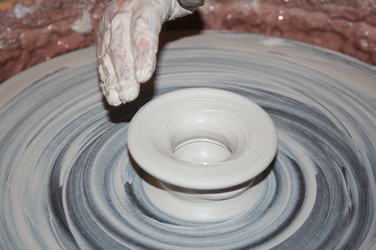 Artisan shapes clay on a spinning pottery wheel, creating a ceramic bowl.