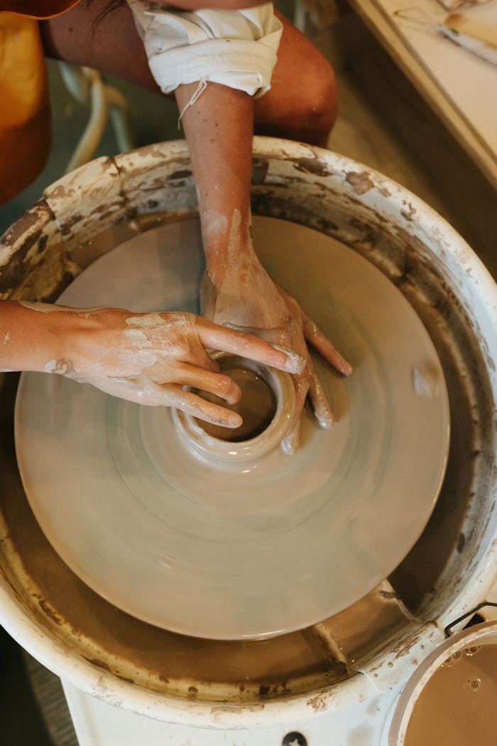 Close-up of hands shaping clay on a potter's wheel, showcasing the art of pottery making indoors.