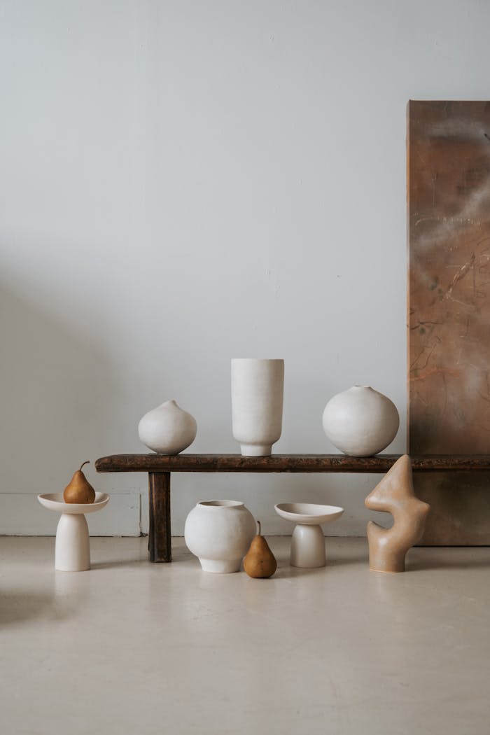 Artistic display of ceramic vases and a wooden bench in a minimalist setting with pears.