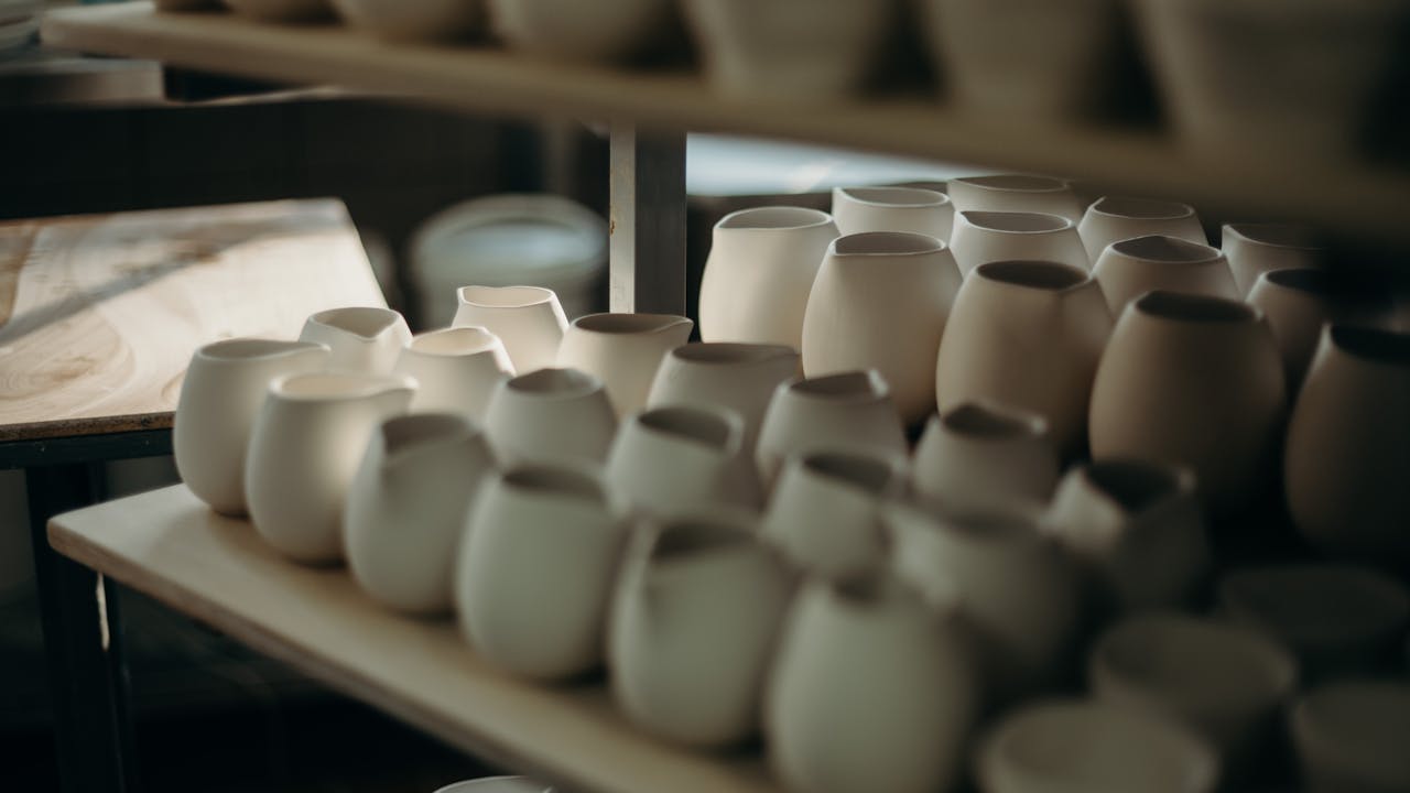 Handcrafted ceramic pots and mugs showcased on wooden shelves with natural lighting.