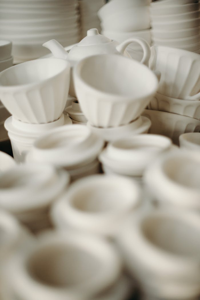 Minimalist white ceramic cups and bowls arranged artistically, showcasing artisanal craftsmanship.