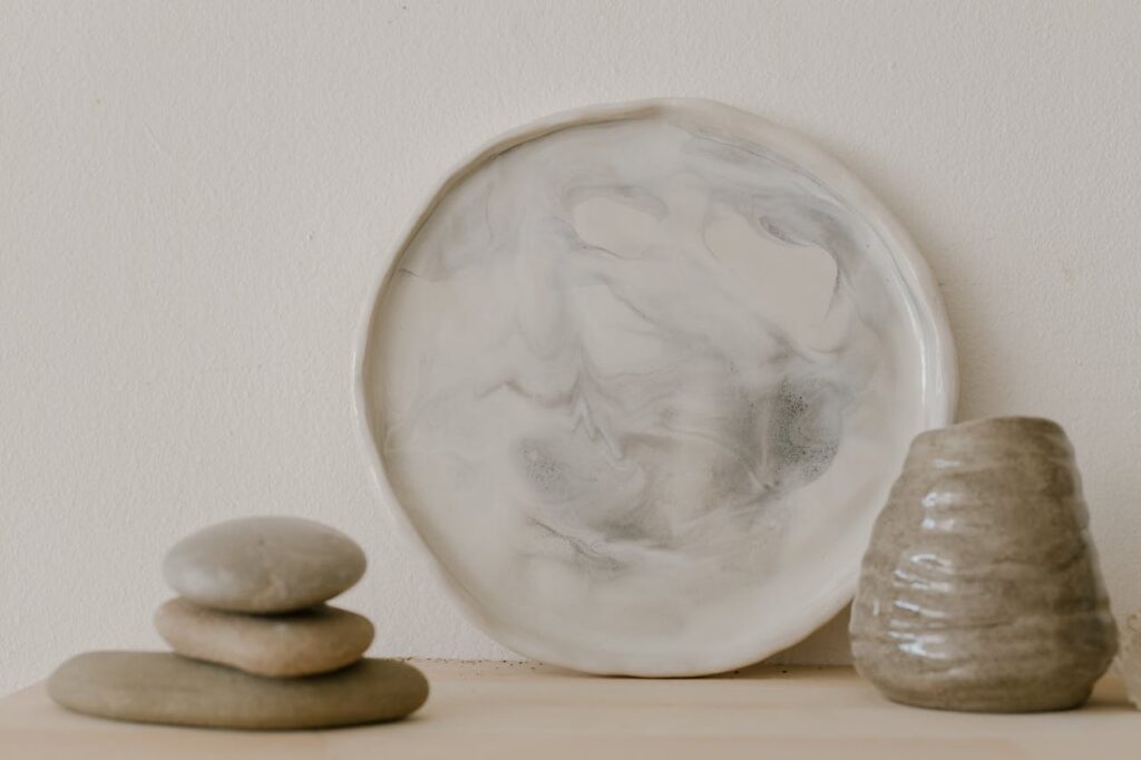 Artistic display of a ceramic plate and vase with stacked stones, showcasing minimalist aesthetics.