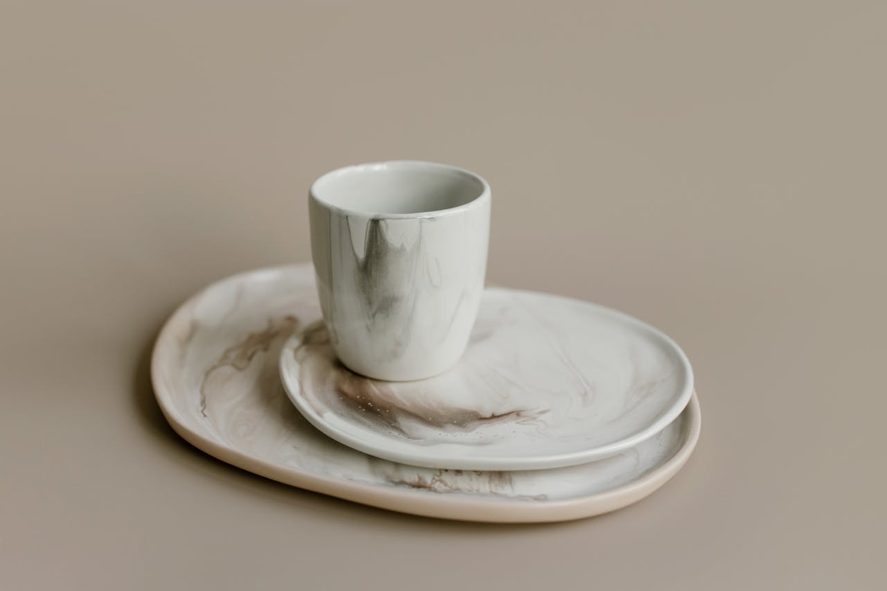 Minimalistic marble-patterned ceramic cup and plates on a neutral background.