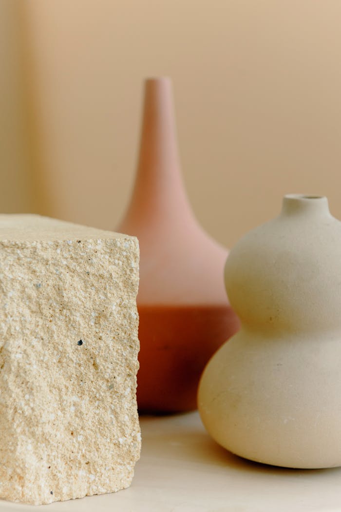 Elegant minimalist still life featuring sculptural vases and a textured stone cube.